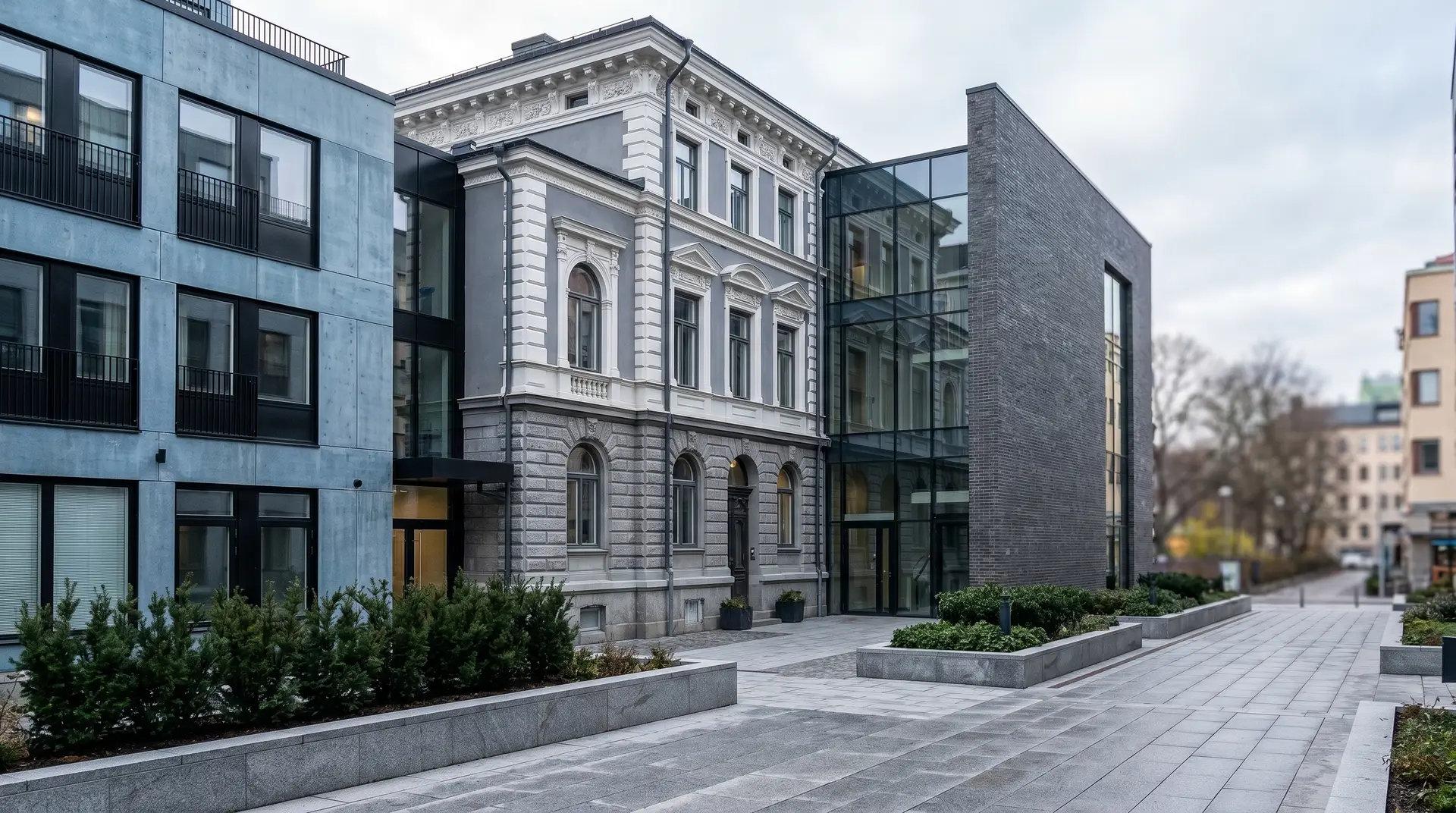 Klassisk vit stenbyggnad integrerad med modern glasarkitektur och gråa betongbyggnader.